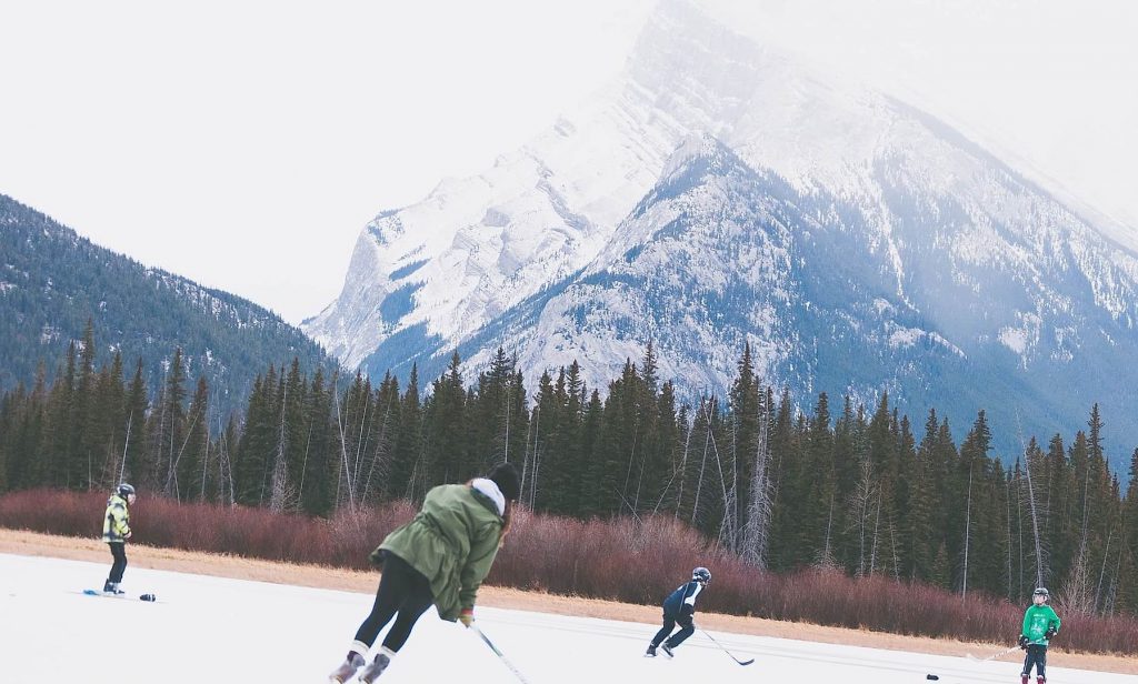 People with kids playing hockey near mountains 